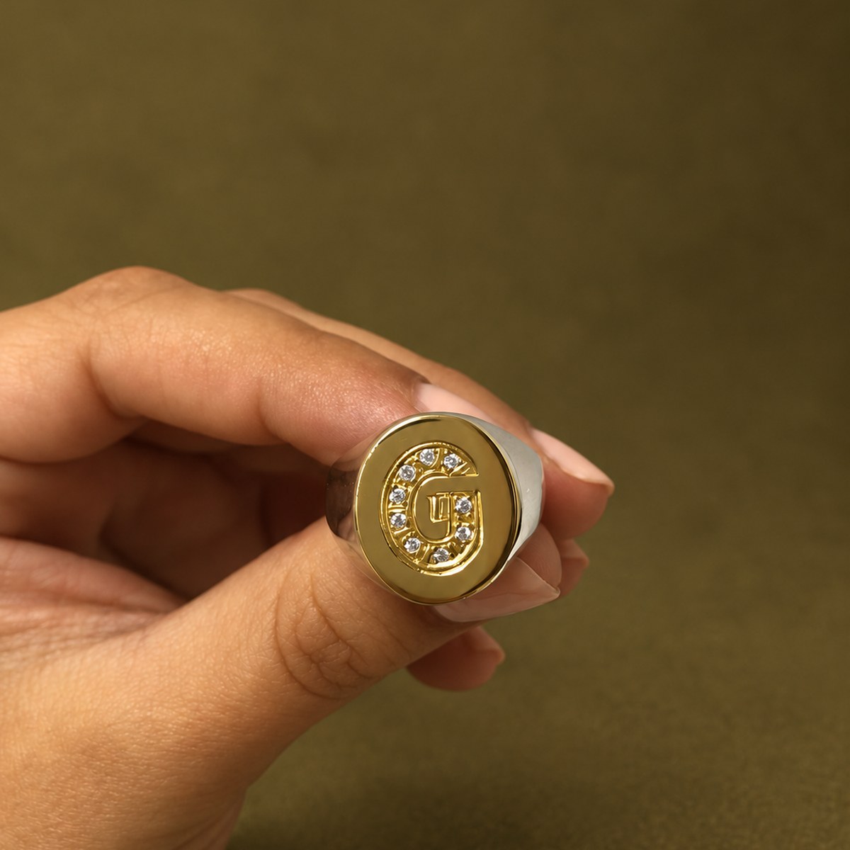 Anillo en oro y plata con la inicial G grabada, sostenido en la mano